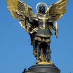 Bronze statue of Archangel Michael with sword and armor in Kyiv, Ukraine under clear blue sky.