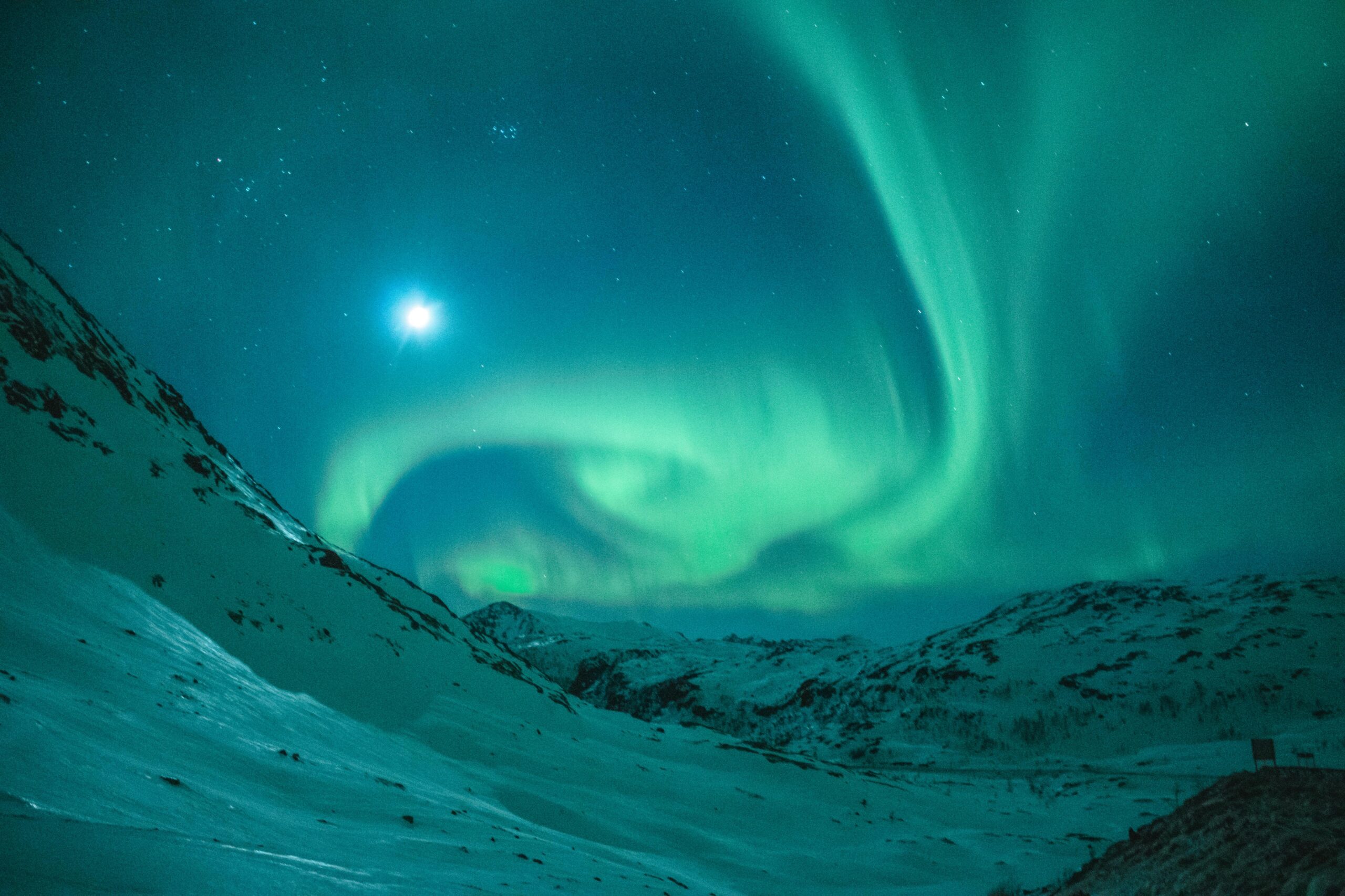 Dazzling aurora borealis illuminating the night sky above a serene snowy mountain landscape.