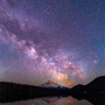 Capture of a brilliant starry night over a serene lake with a mountain peak reflection, creating a magical scene.